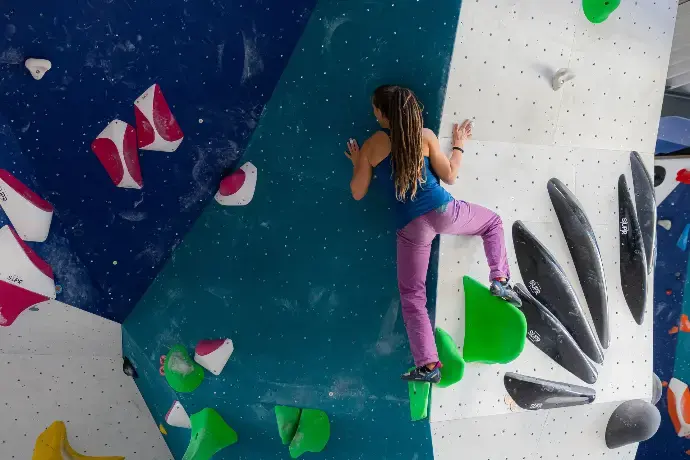 Climber balancing between teal and white walls with green and black volumes