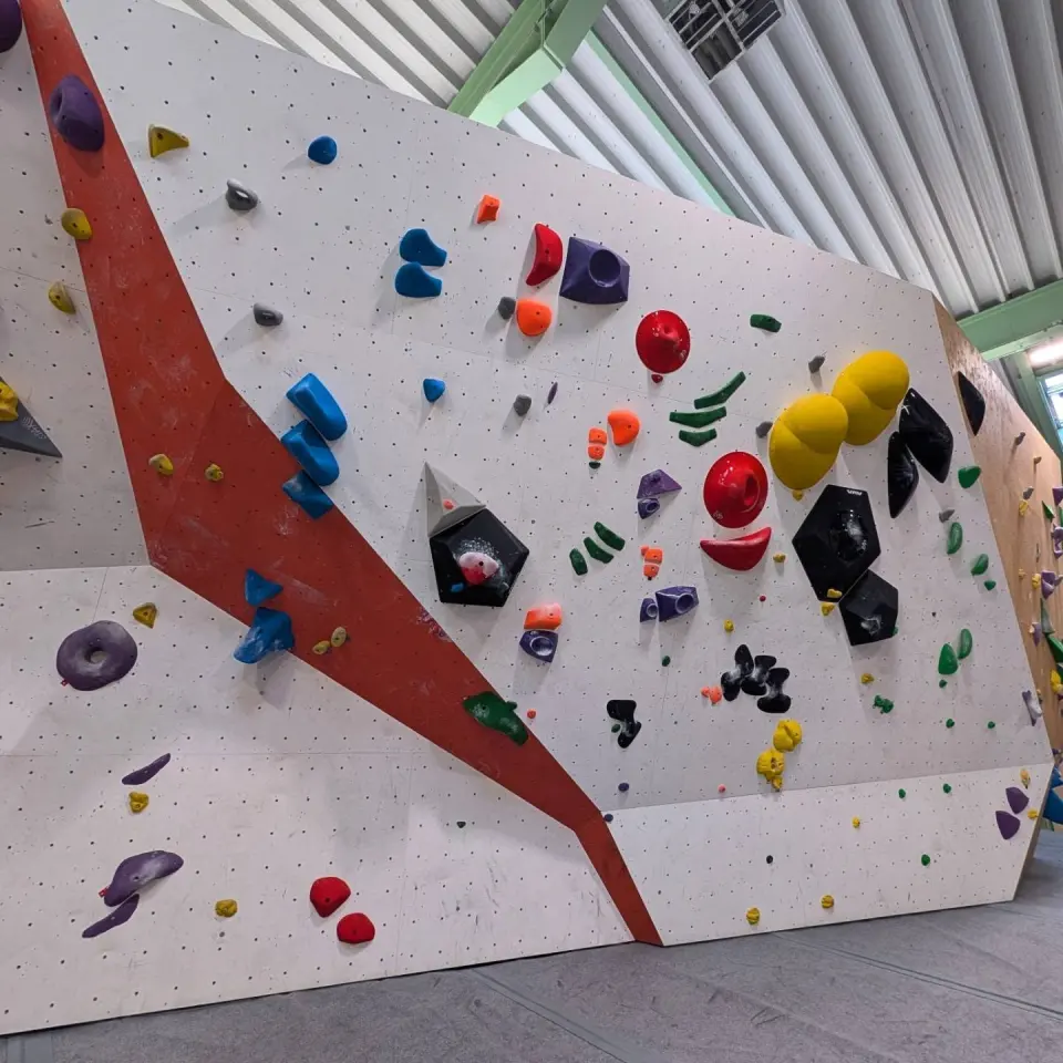 A white bouldering wall set with colourful holds and volumes