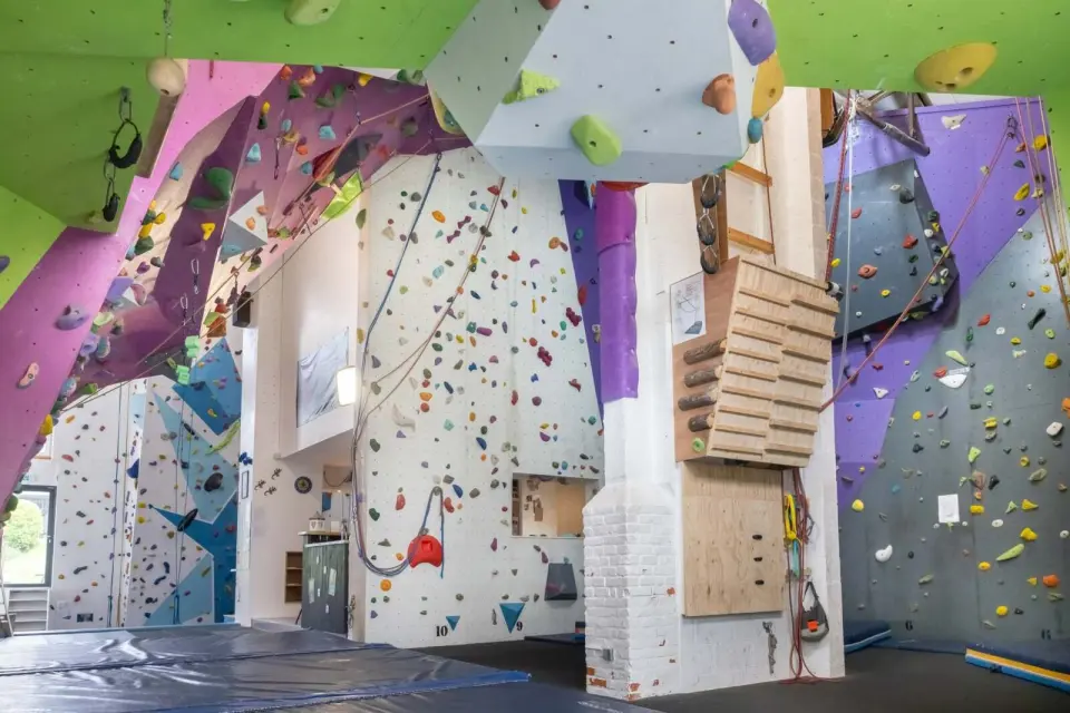Roped walls and overhangs in the ESKIlibre hall, with a wooden training board and mats