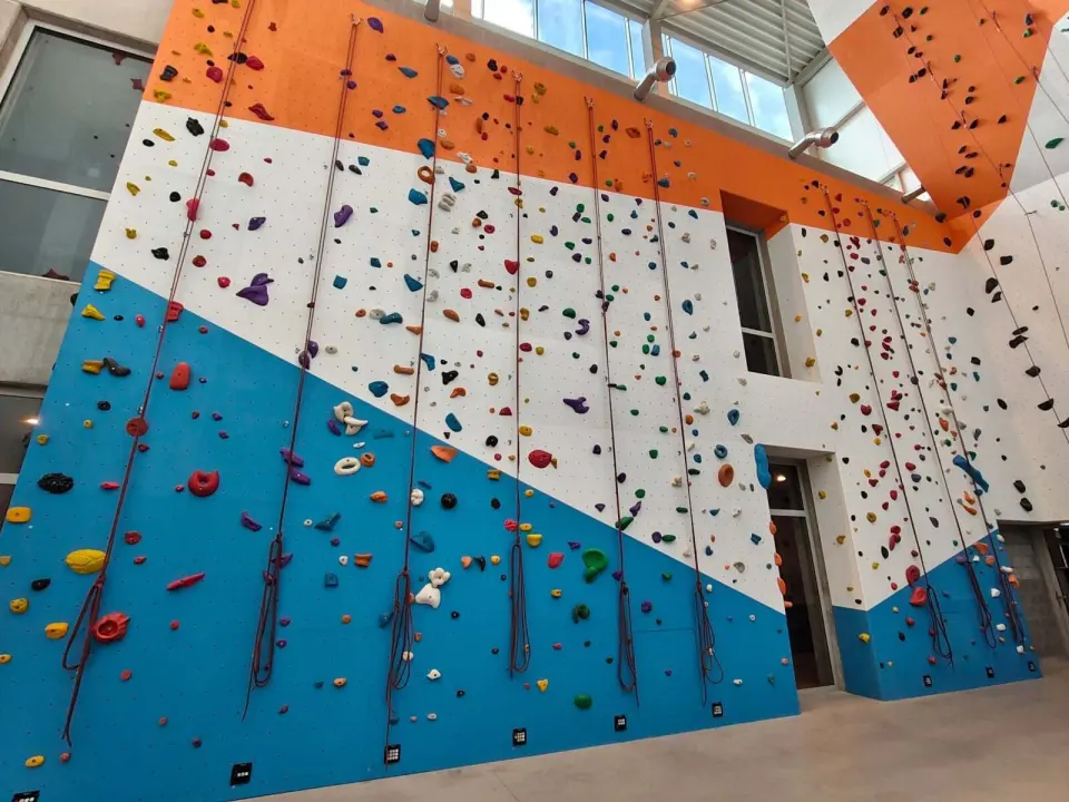 Blue, white and orange roped walls under the glass roof of the climbing hall