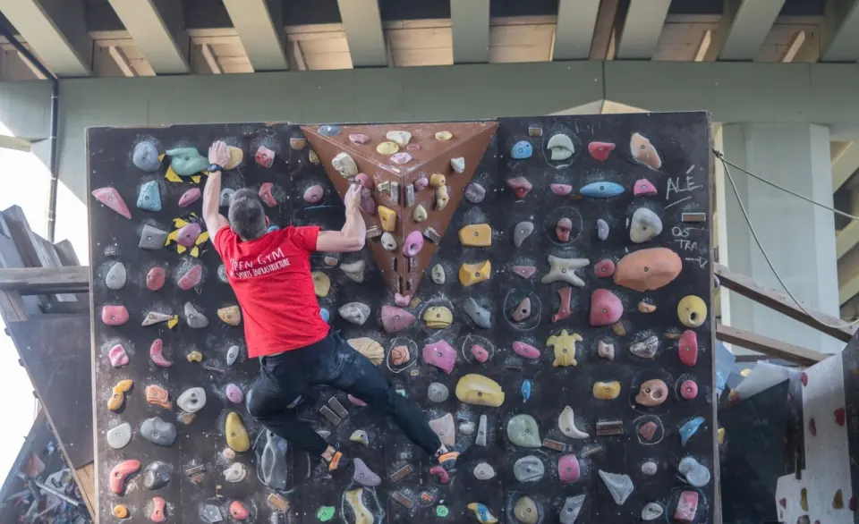 Climber on a home-made spray wall packed with holds, under the motorway bridge