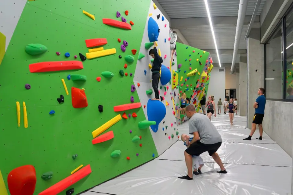 Long green and white bouldering wall with bright holds and volumes above thick grey crash mats
