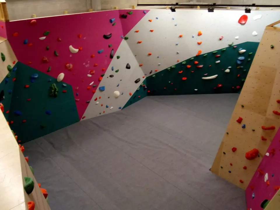 Bouldering room with pink, white and green walls above grey crash mats