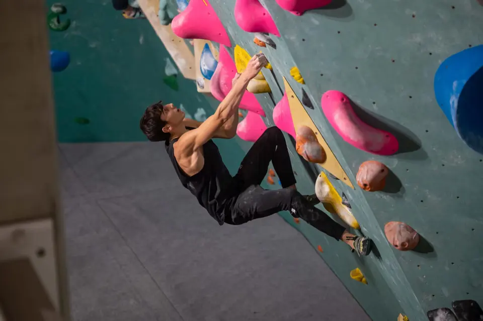 Climber reaching between pink holds on the turquoise bouldering wall