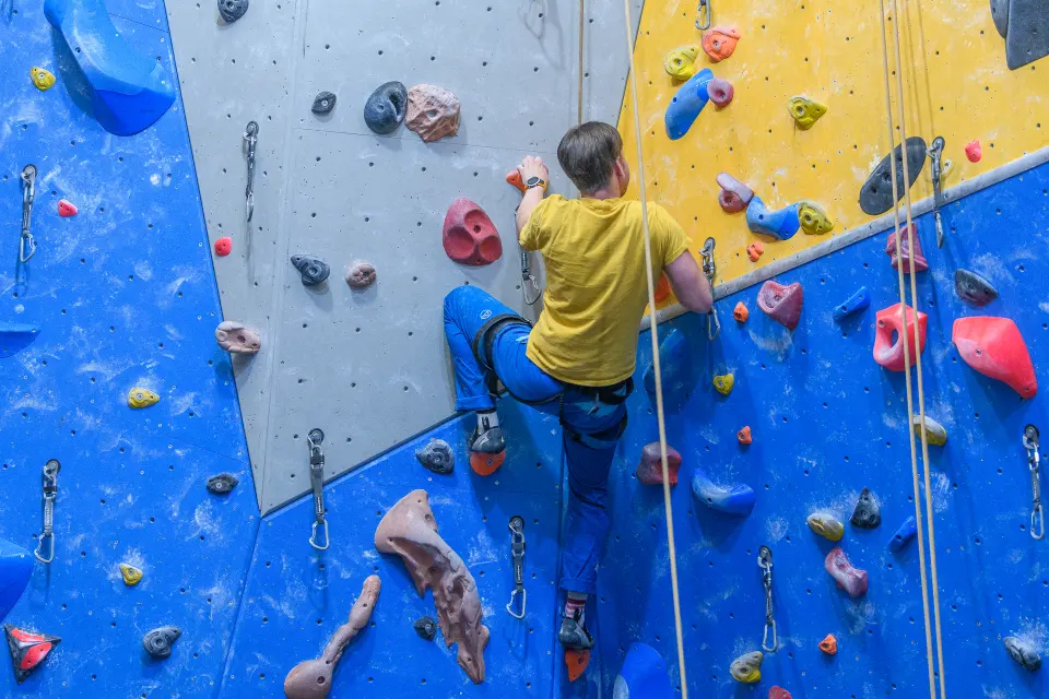 Climber on a blue panel with quickdraws in place