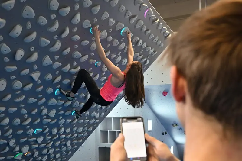Climbing the Kilter Board while a friend picks a problem in the app