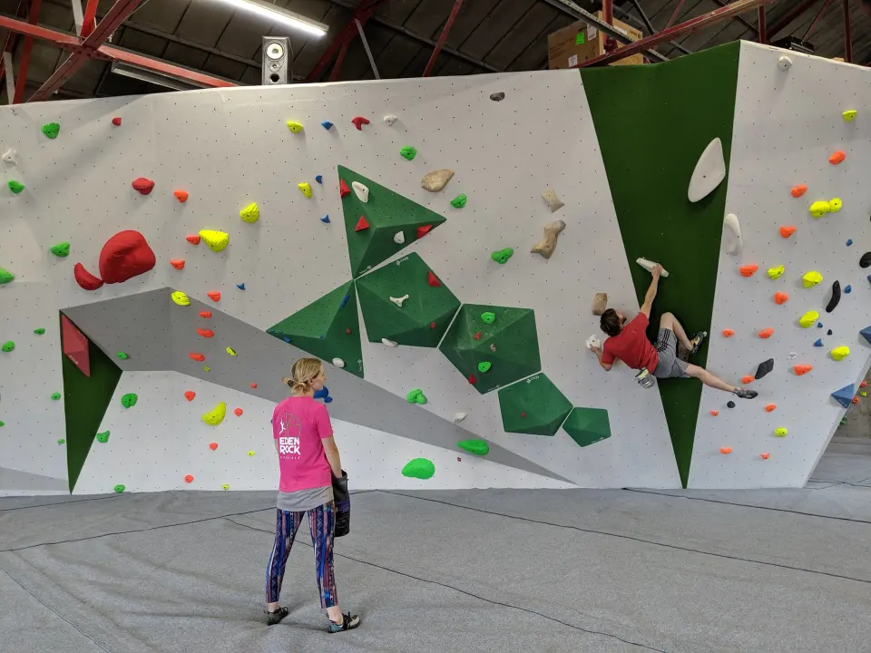 Long white bouldering wall with green volumes above grey matting