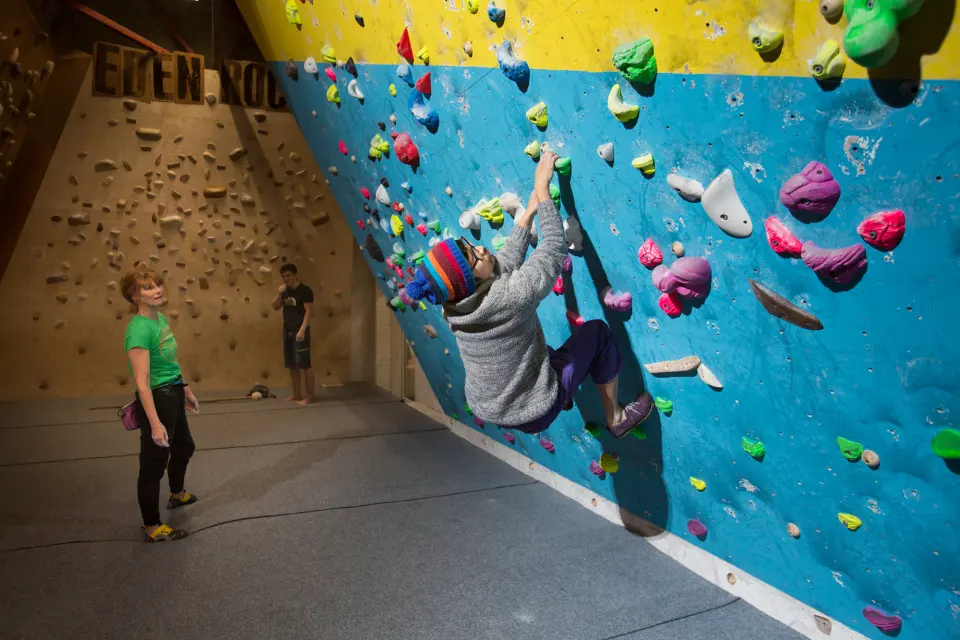 Climber on the blue and yellow wall, with a wooden board behind