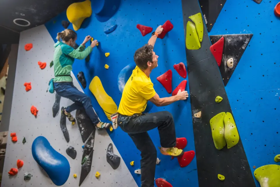 Climbers on a blue bouldering wall with big volumes