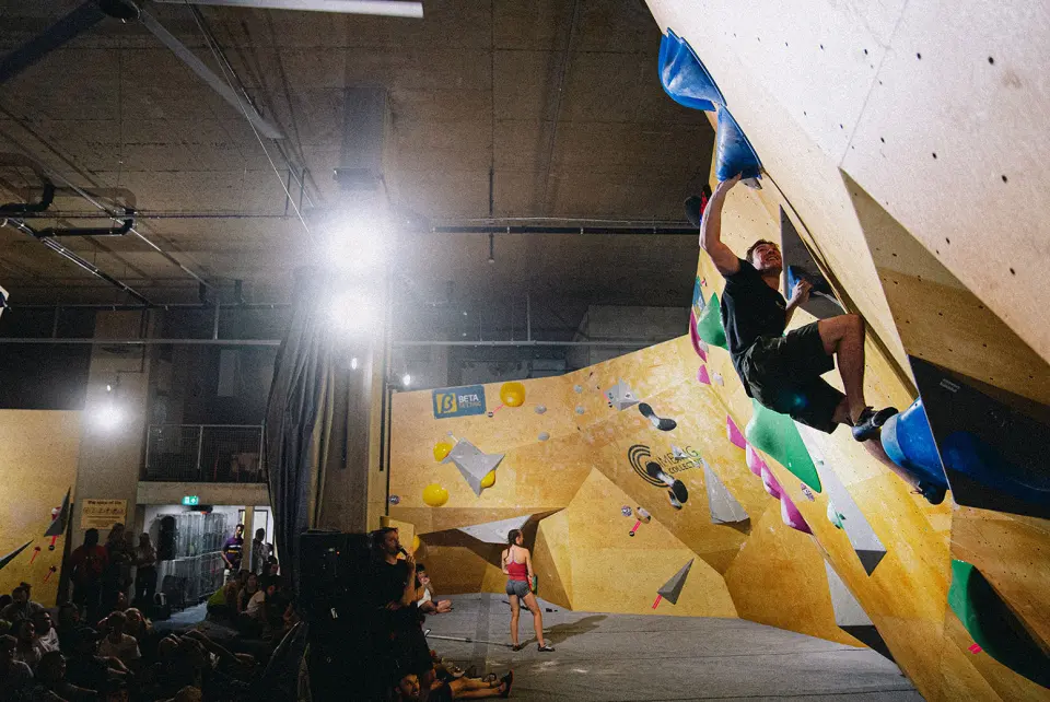 Climber on a steep wooden bouldering wall under bright lights