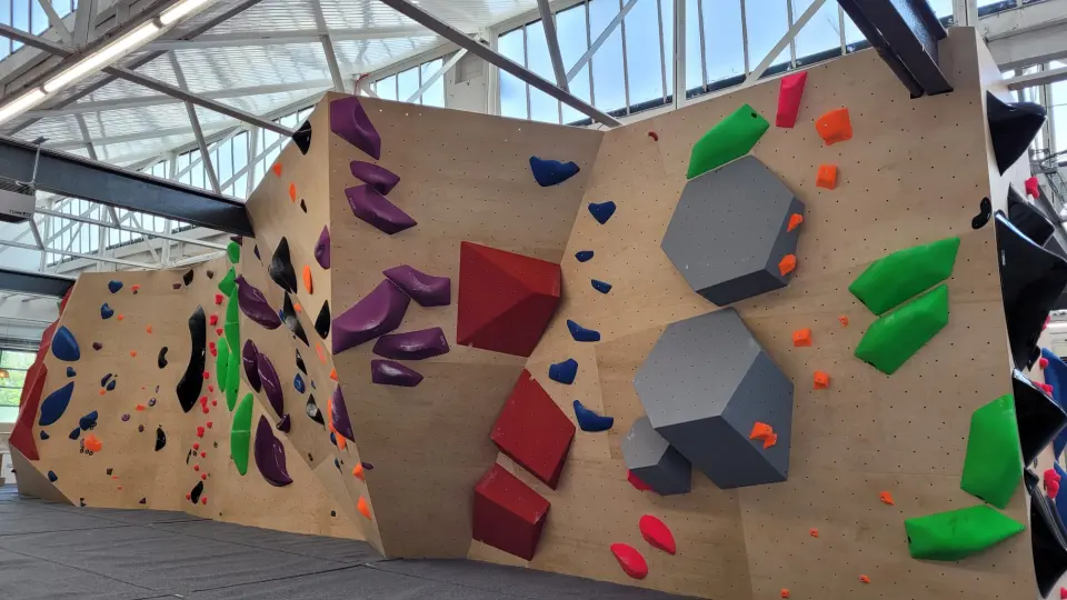 Bouldering wall with grey and red volumes under a skylit roof