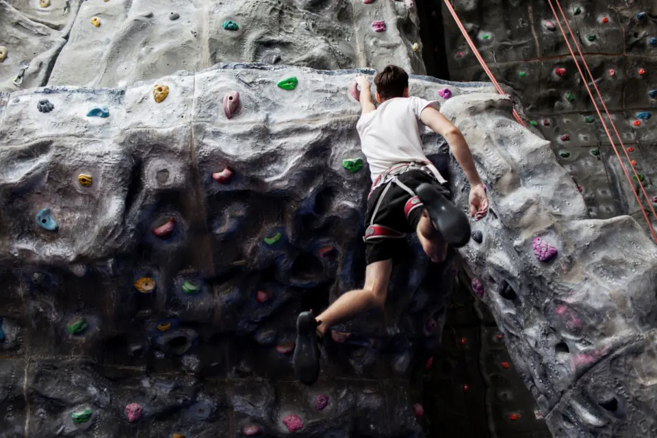 Climber moving over a bulge on the grey roped wall