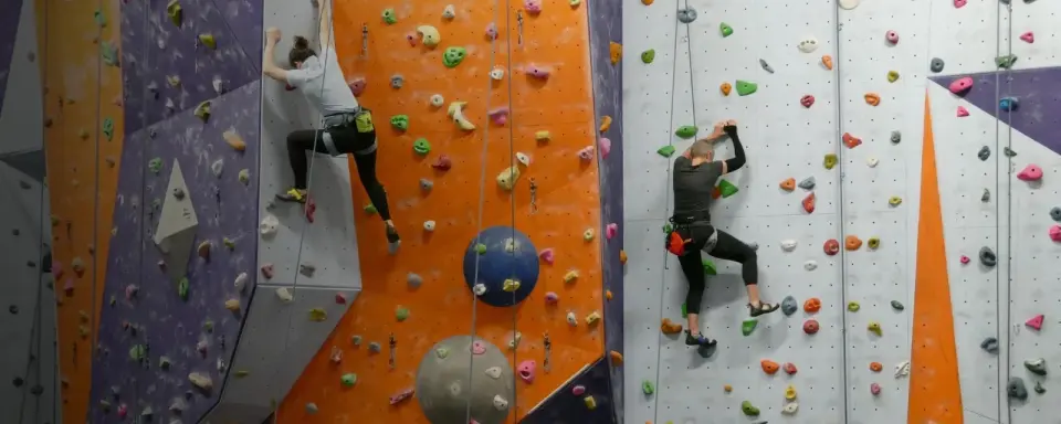 Two climbers on top ropes on the orange and white walls