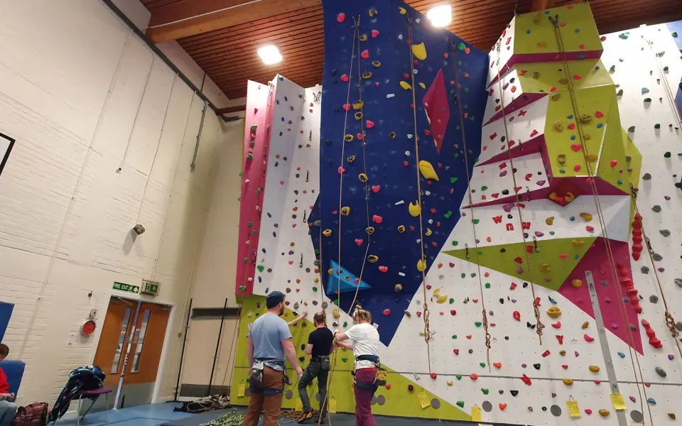 Roped climbing wall with blue and lime-green roof sections in the school sports hall