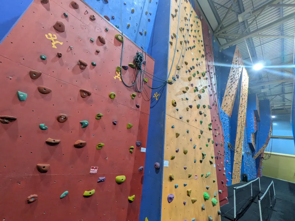 Red and timber-effect roped climbing walls with quickdraws in the sports hall