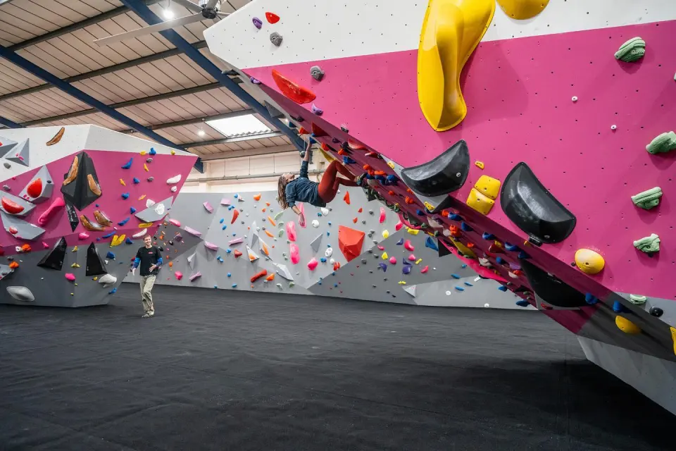 Climber on a pink overhang above the matted bouldering hall