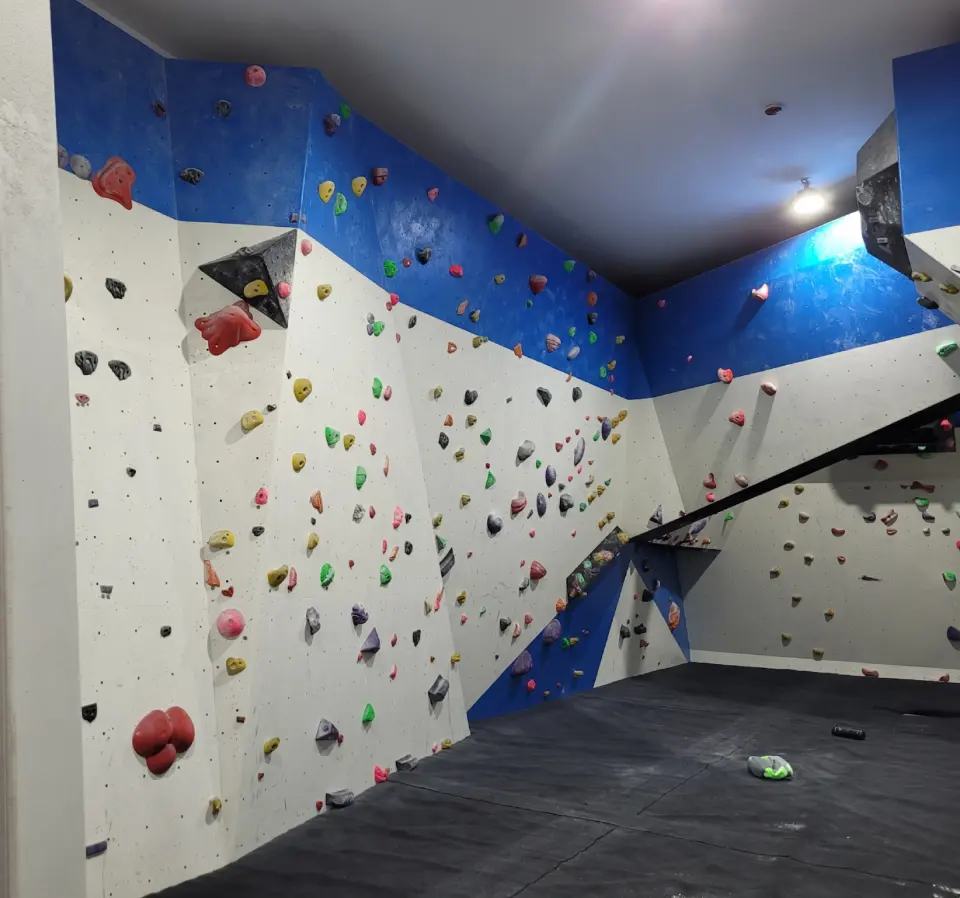Corner of the bouldering room with overhanging blue panels and coloured holds