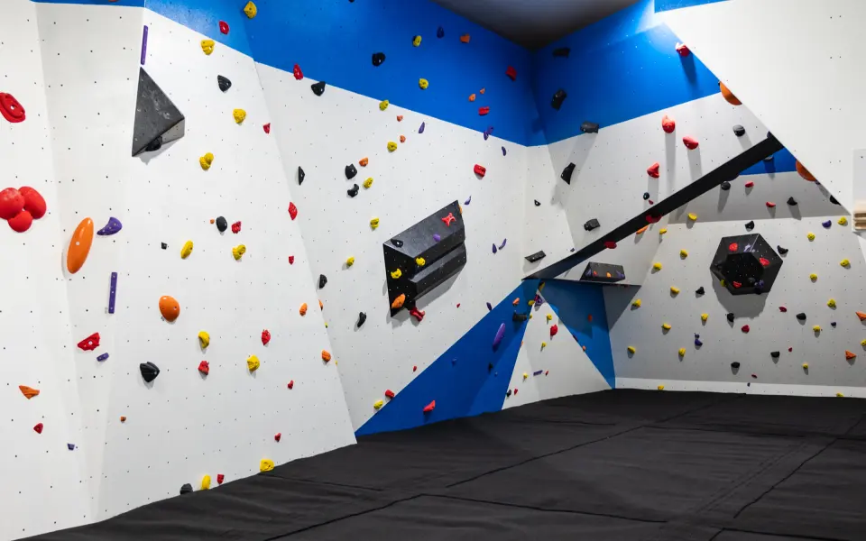 Blue and white bouldering walls with black volumes above thick matting