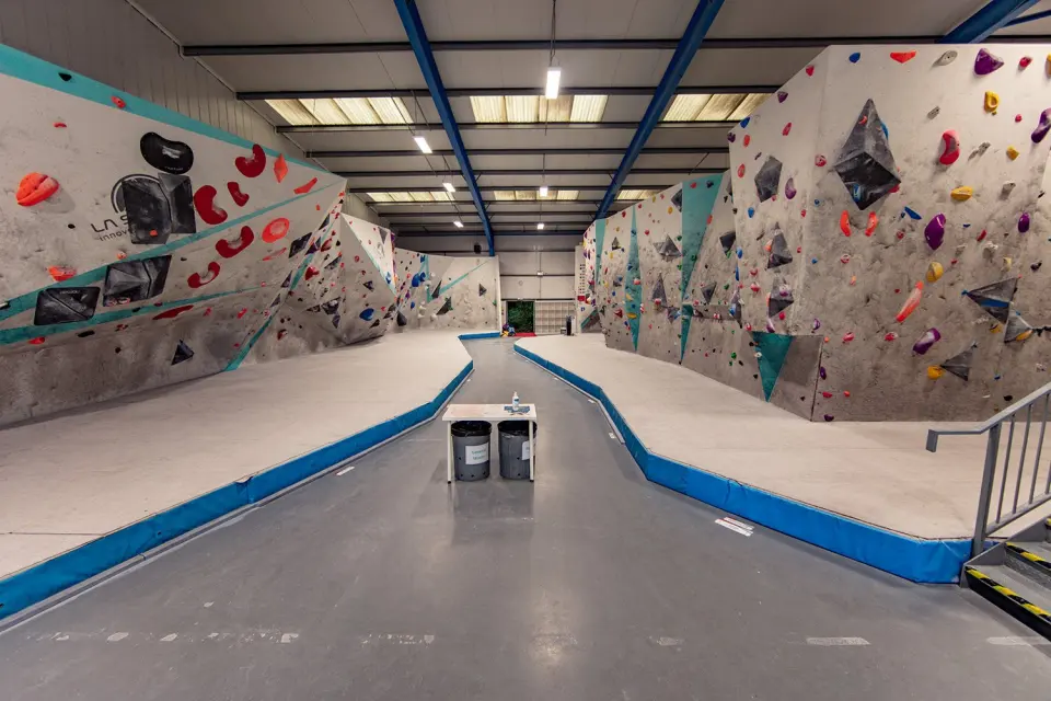 Long aisle between grey bouldering walls with blue padded matting