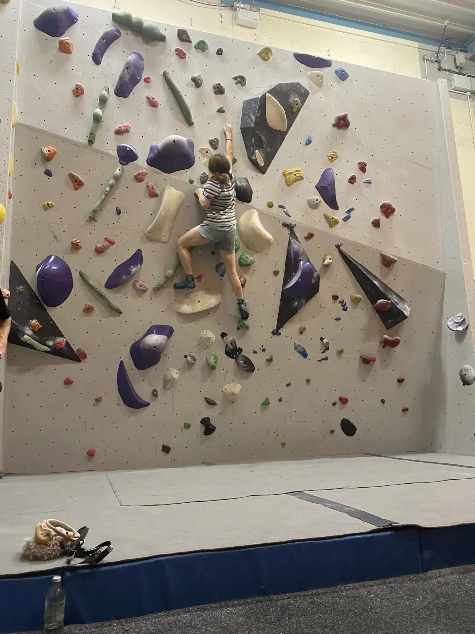 Climber on a grey bouldering wall with purple volumes