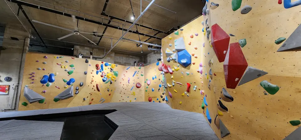 Bouldering walls with yellow panels and big volumes under the exposed ceiling