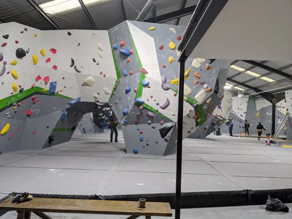 Long bouldering wall with grey and green panels above the matted floor