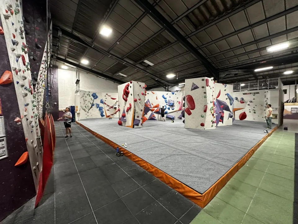 Bouldering hall with freestanding boulders and grey matting under the warehouse roof