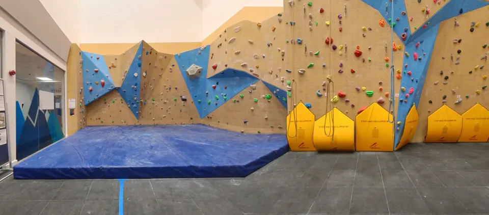 Bouldering corner with blue crash mat beside the tall roped walls