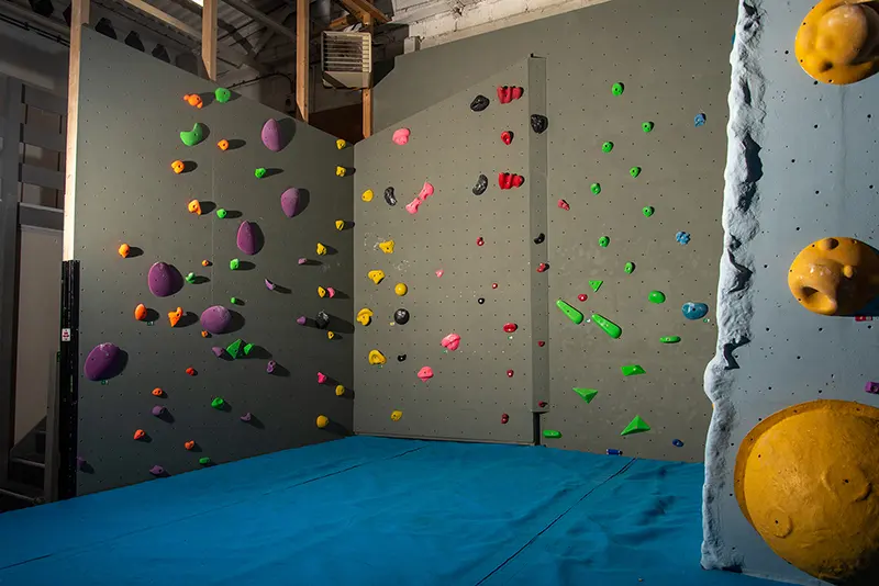 Grey bouldering walls in a corner above blue matting