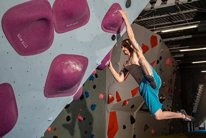 Climber reaching between large pink volumes on a steep wall