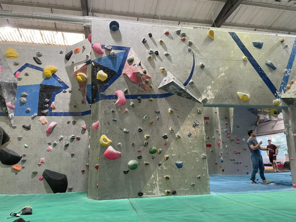 Grey bouldering walls with blue stripes and volumes above green matting