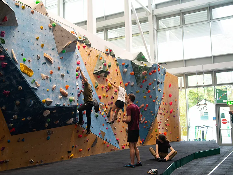 Climbers on the blue and orange bouldering wall beside the sports village windows