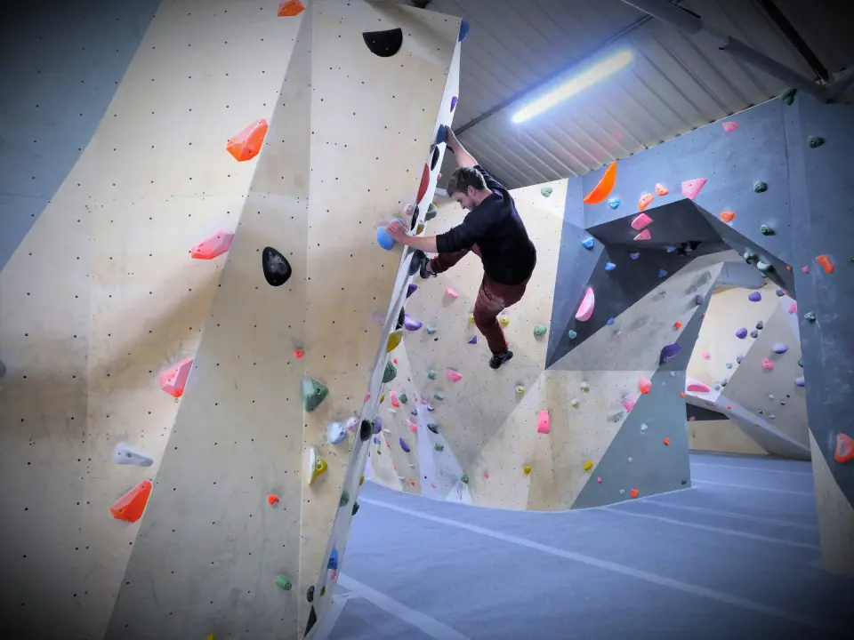 Climber on an angled bouldering wall with grey overhangs behind