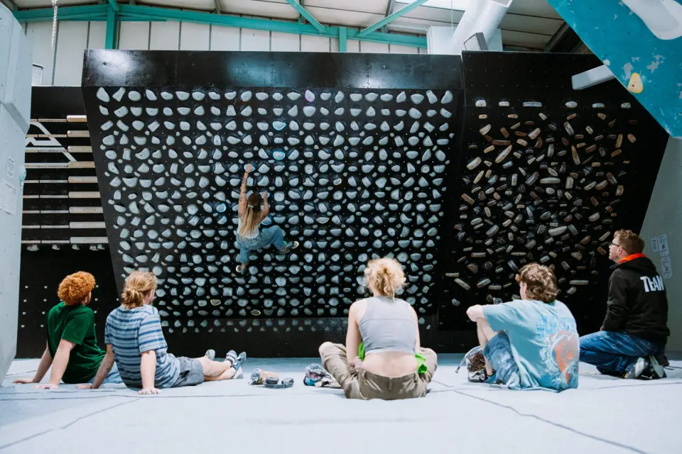 Climbers sitting on the mats watching a climber on the black board