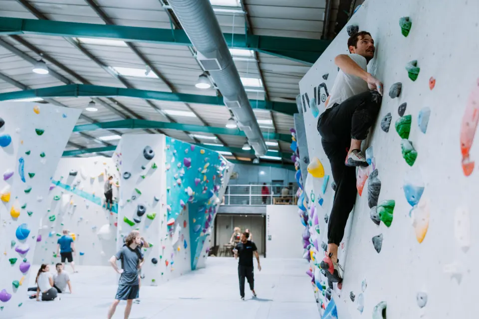 Climbers on the white and teal bouldering walls under the green roof beams