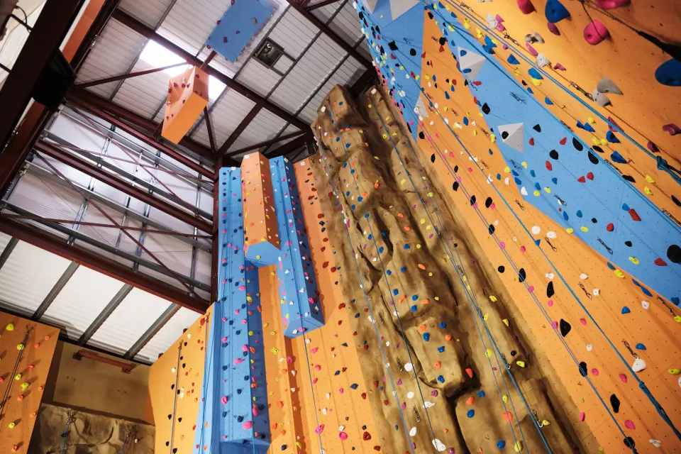 Looking up the tall orange and blue climbing wall under the roof