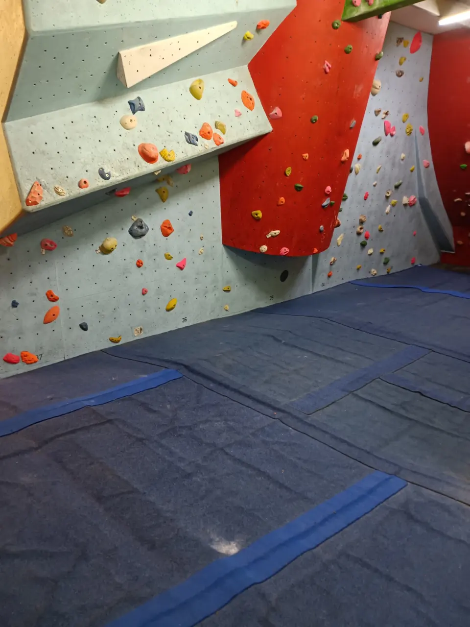 Bouldering room with grey and red walls over blue mats