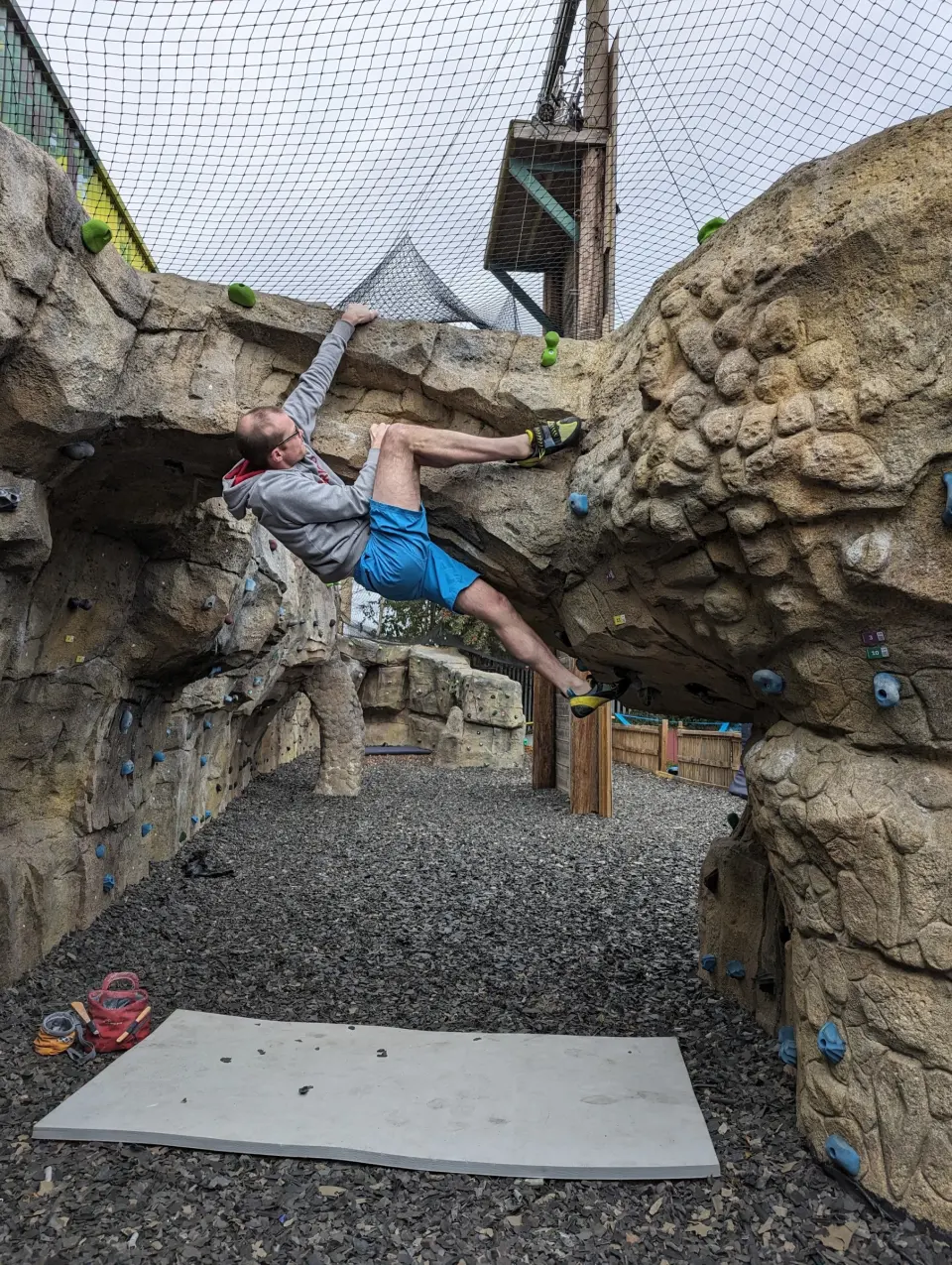 Climber hanging between two rock boulders above a crash pad