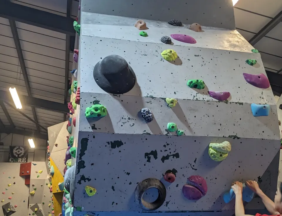 Grey bouldering tower with big volumes and holds, under the warehouse roof