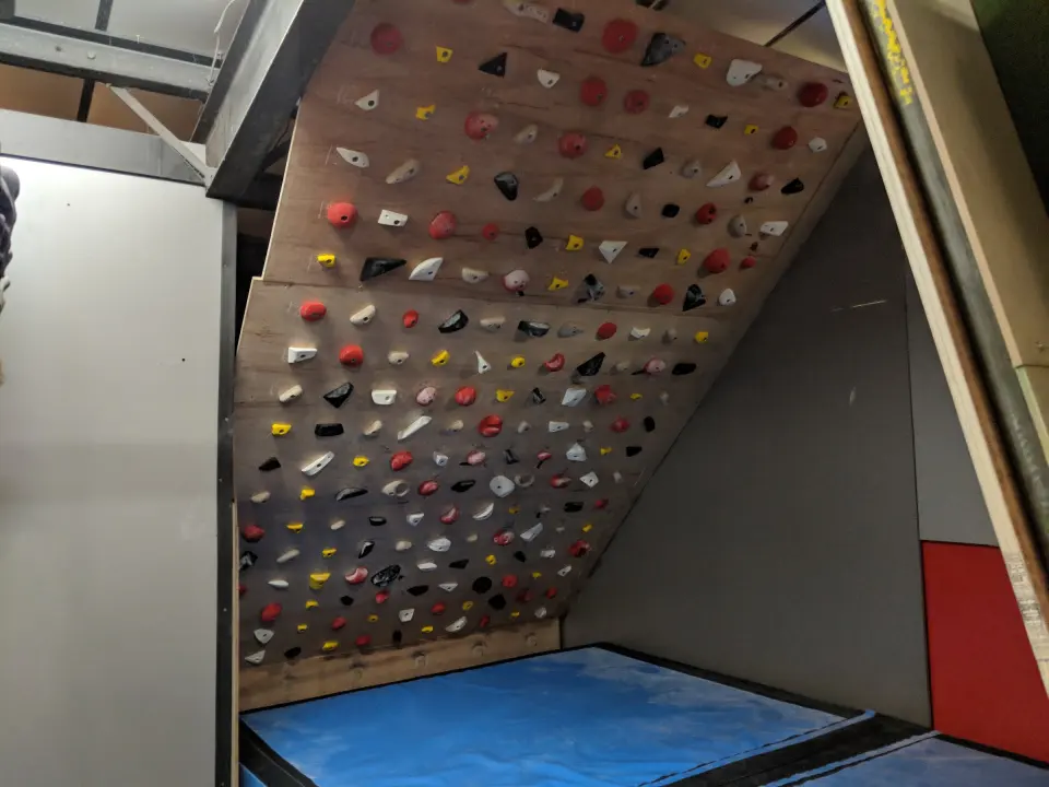 Wooden training board covered in holds above blue matting