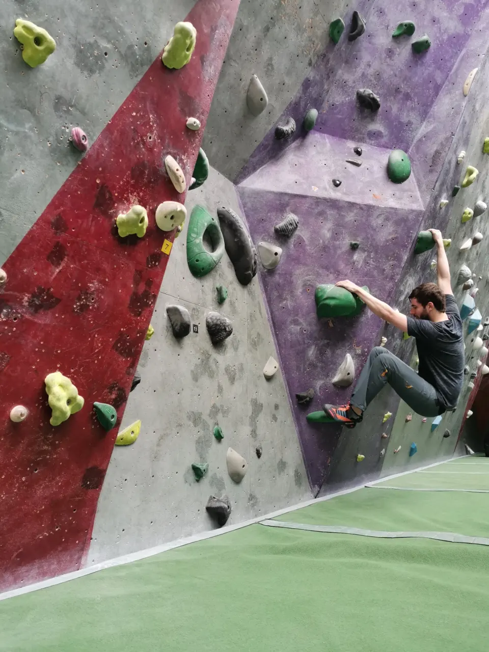 Climber on a red and purple wall with big green holds