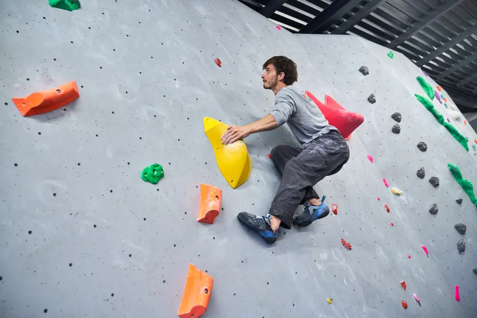 Climber on a grey wall with orange and yellow volumes