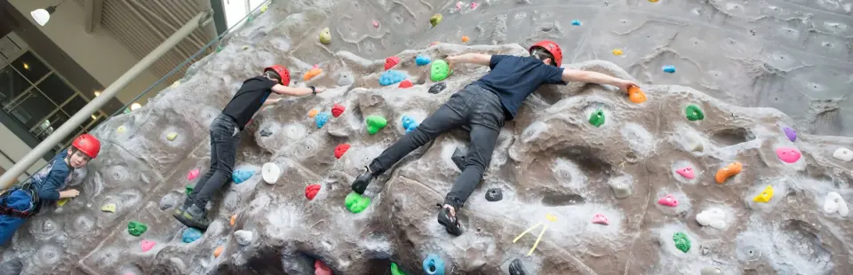 Young climbers in helmets on the grey featured climbing wall