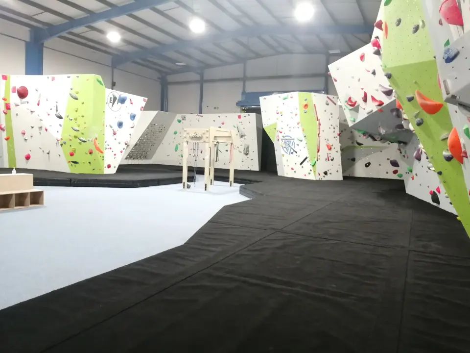 Bouldering hall with white and green walls, a free-standing boulder and black matting