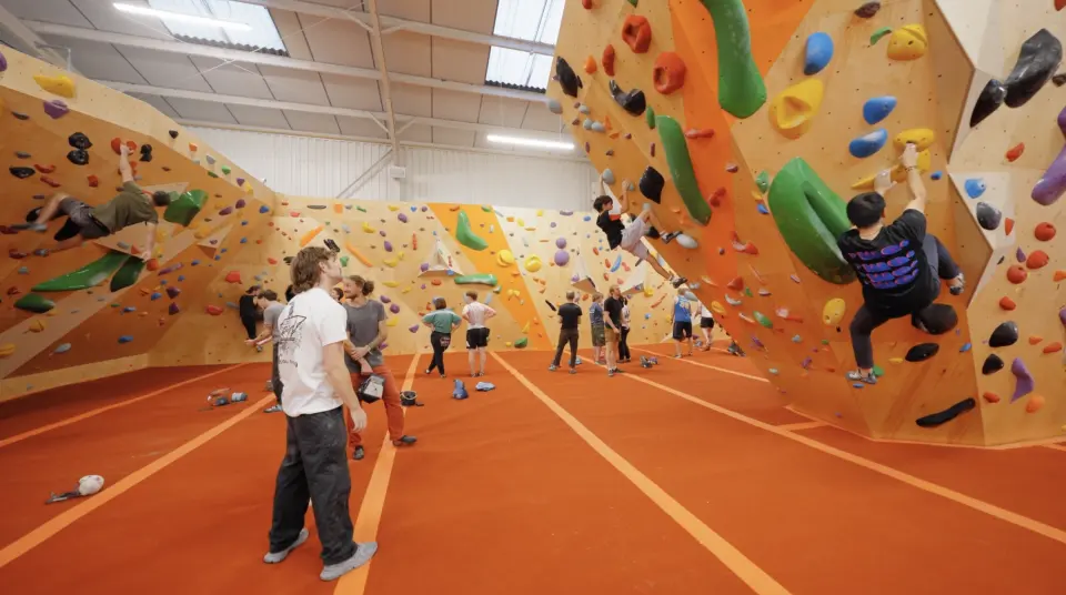 Climbers on orange bouldering walls above red matting