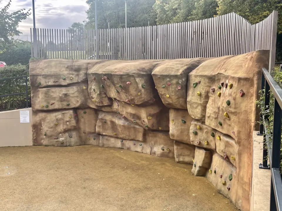 Curved rock-effect outdoor bouldering wall with coloured holds above a rubber surface