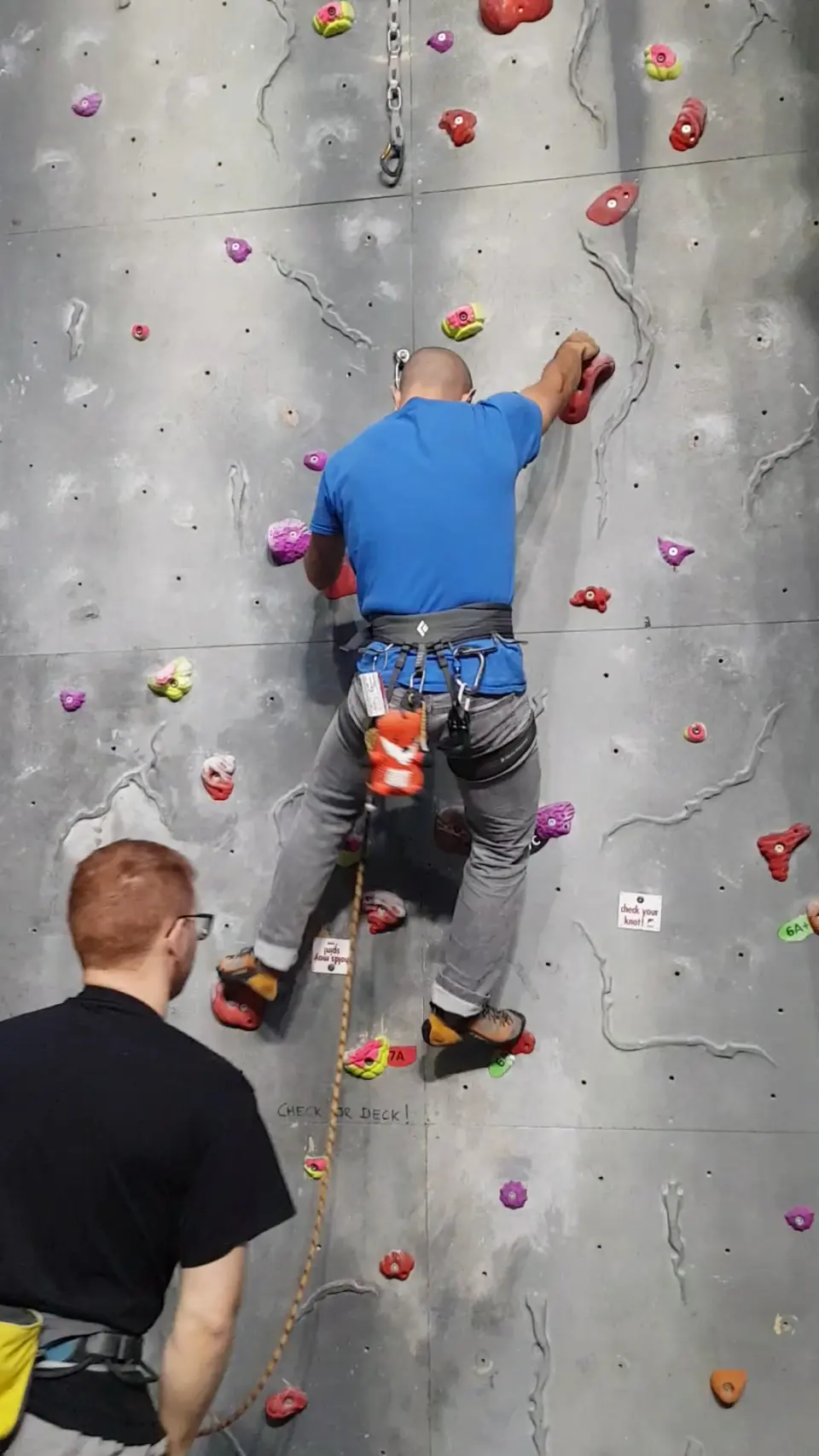 Climber on a vertical roped wall with a belayer below