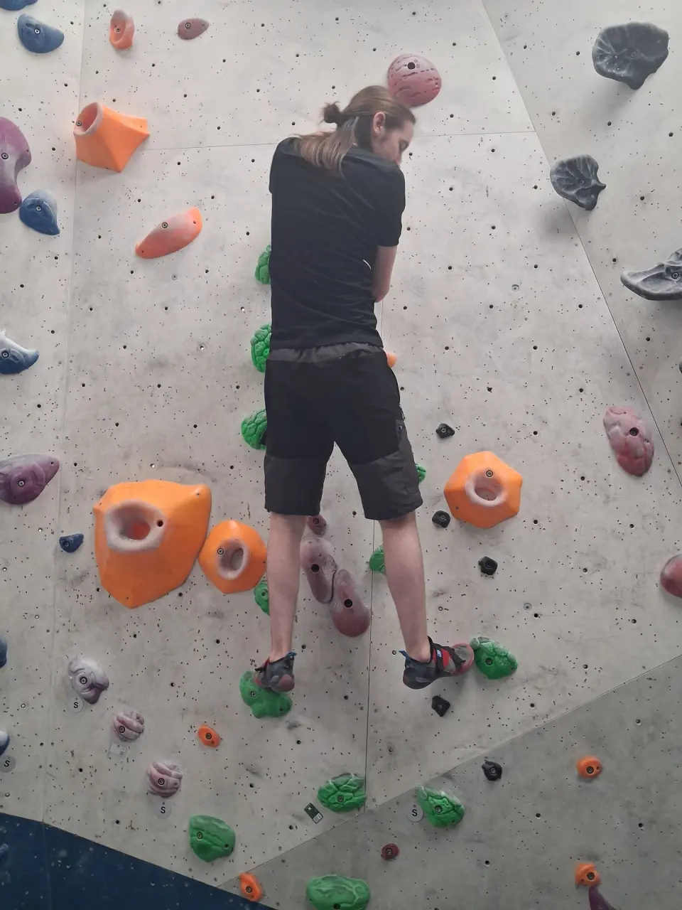 Climber on a grey wall with orange volumes and green holds