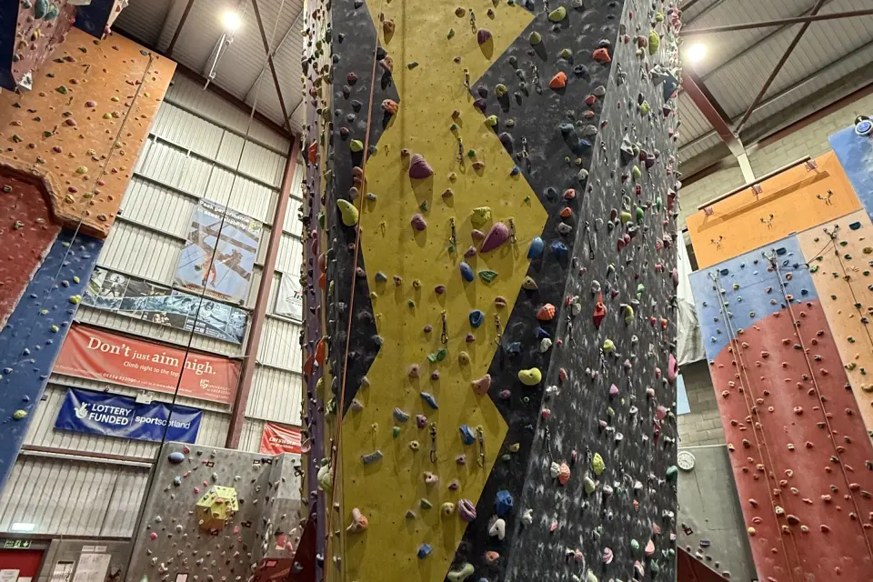 Tall roped climbing tower painted yellow and grey between orange and red walls