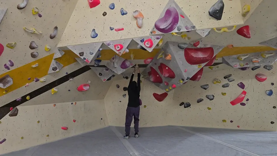 Angular white bouldering walls over grey matting under strip lights